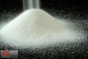 A Mountain of Granulated Sugar on a Black Background - Pure, snowy white mountain of sugar on a black textured background with a soft mist of sugar granules falling on the top.